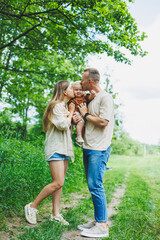 Fototapeta premium A family couple with a small son are standing in the park on the grass. Mother, father and child walk. Happy family with a child.