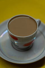 A mug of coffee with milk. Mug in a saucer on a yellow background. Top-down view