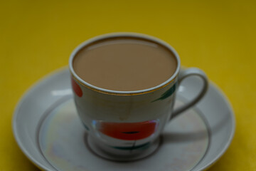 A mug of coffee with milk. Mug in a saucer on a yellow background. Top-down view