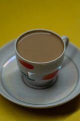 A mug of coffee with milk. Mug in a saucer on a yellow background. Top-down view