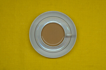 A mug of coffee with milk. Mug in a saucer on a yellow background. Top-down view