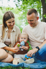 A family of a mother and father with a child in their arms, sitting in the park in the summer. The concept of a happy family with a small child, care and love. Happy family with a child.