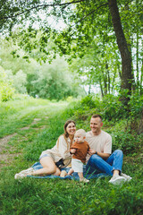 Fototapeta premium A family of a mother and father with a child in their arms, sitting in the park in the summer. The concept of a happy family with a small child, care and love. Happy family with a child.