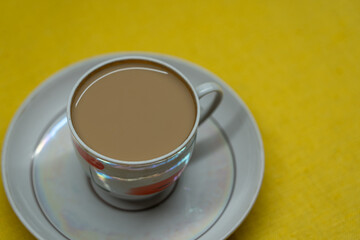 A mug of coffee with milk. Mug in a saucer on a yellow background. Top-down view