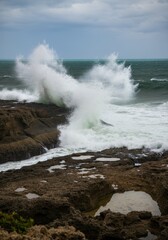Dramatic ocean wave crashing against rocky shoreline on a cloudy day
