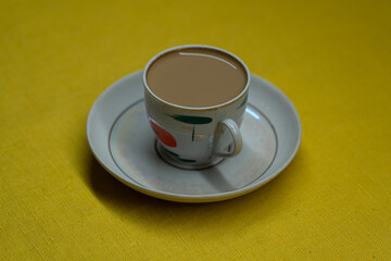 A mug of coffee with milk. Mug in a saucer on a yellow background. Top-down view