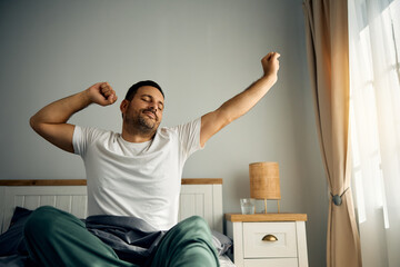 Man stretching in his bed after waking up in morning.