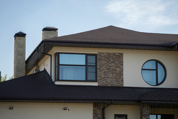This sleek modern house features large glass windows and a unique roof design, nestled amidst lush green trees on a sunny day, providing a peaceful ambiance in the neighborhood