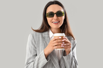 Young woman in stylish suit with cup of coffee on light background, closeup