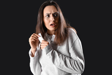 Worried female junkie with drugs on black background