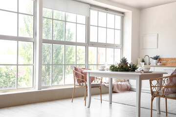 White dining table with champagne glasses, burning candles and Christmas wreath in kitchen