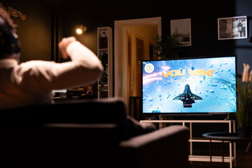 Gamer celebrating after winning gaming console game displayed on ultrawide smart TV. Man in apartment bragging after being victorious in videogame, completing level using gamepad