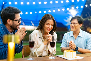Group of Happy Asian millennial people friends enjoy and fun celebration birthday party at dinner party the garden at restaurant. Beautiful woman excited with birthday cake and blowing candle.