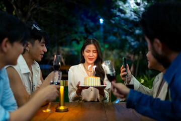 Group of Happy Asian millennial people friends enjoy and fun celebration birthday party at dinner party the garden at restaurant. Beautiful woman excited with birthday cake and blowing candle.