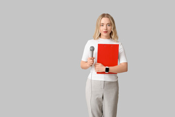 Fototapeta premium Portrait of female journalist with microphone and clipboard on grey background