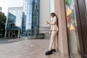 Urban Elegance: A Stylish Young Woman in Business Attire Engaged in Her Phone in a Modern Cityscape