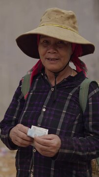 mature vietnamese woman with a big hat on her head counts the money she has in her hands after a payment