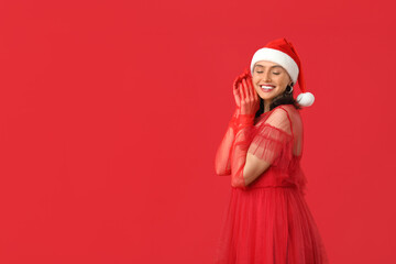 Beautiful young woman in Santa hat on red background