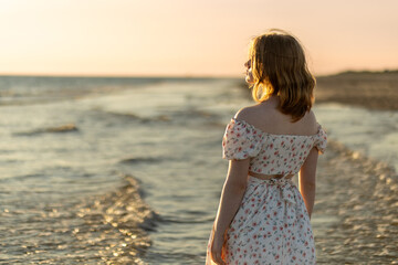 A girl in a floral dress enjoying the sunset by the calm seaside waves in a serene coastal location...