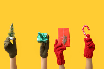 Female hands in warm gloves with Christmas gifts and decorations on yellow background