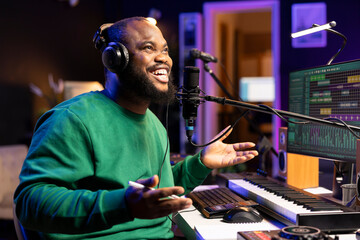 Cheerful composer producer recording a new song in home studio, using audio equipment and microphone to add acoustics on tracks. Young singer artist composing music for an album.