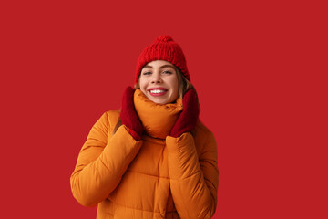 Beautiful young happy woman in warm winter clothes on red background