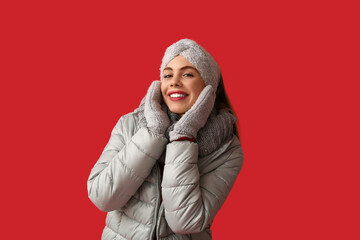 Fototapeta premium Beautiful young happy woman in warm winter clothes on red background