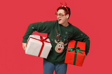 Handsome young man in warm sweater with gift boxes on red background
