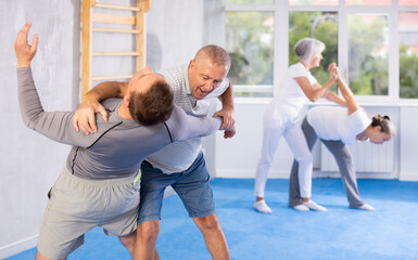 Obraz premium Mature man at a self-defense lesson learns how to make painful blows with his hand and foot