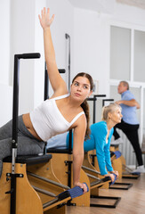 Fototapeta premium Positive sporty young female in activewear performing side bends during workout on Pilates Wanda chair machine in gym