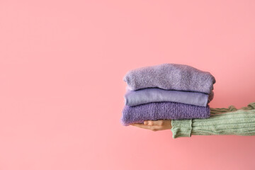 Woman with folded sweaters on pink background