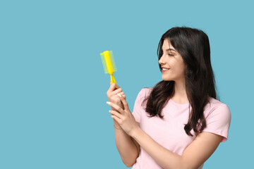 Beautiful young woman with yellow hair brush on blue background