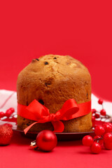 Plate with tasty Panettone and Christmas decor on red background