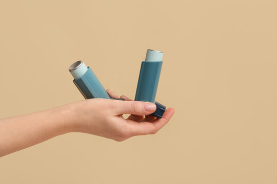 Female hand with modern asthma inhalers on beige background