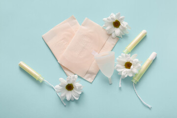Menstrual pads with tampons, cup and chamomile flowers on blue background