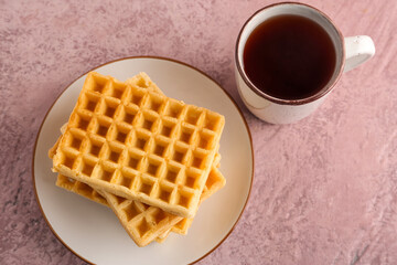 Plate with delicious Belgian waffles and cup of tea on pink background