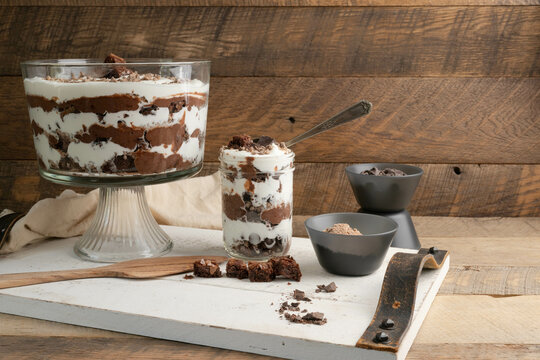 Chocolate brownie trifle bowl with ingredients on white tray in a rustic kitchen.