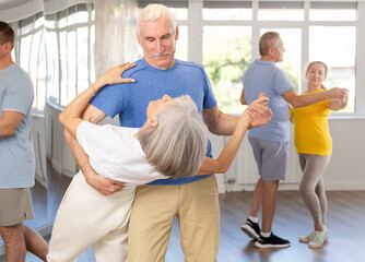 Group of elderly pensioners learn to dance a couple tango dance in a dance class