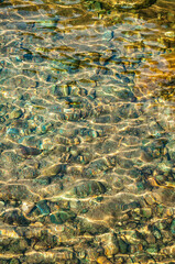 clear water with pebbles and shiny rocks under a river in the sun between turquoise and green tones, for backgrounds and textures