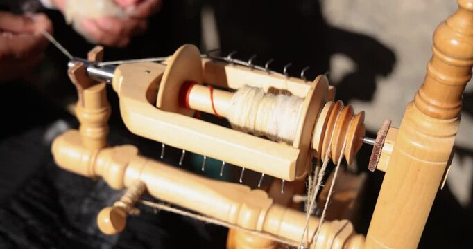 Close up slow motion captures a craftsman skillfully spinning wool on a traditional spinning wheel, showcasing intricate techniques. Selective focus