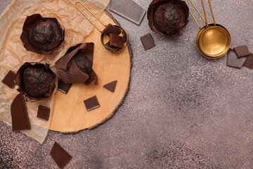 Wooden board with tasty chocolate muffins and measuring cups on grey grunge background