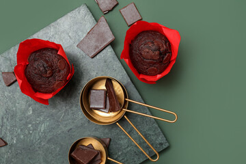 Board with tasty chocolate muffins and measuring cups on green background