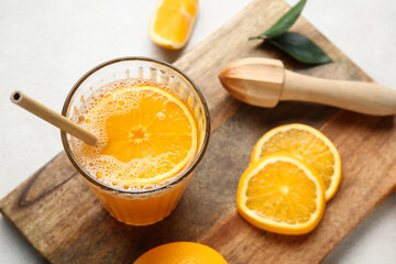 Wooden board with glass of tasty juice and orange slices on white background