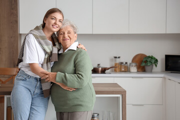 Happy senior woman and her granddaughter hugging in kitchen at home
