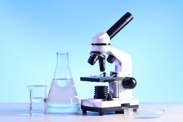 Modern microscope and laboratory glassware with liquid on white table