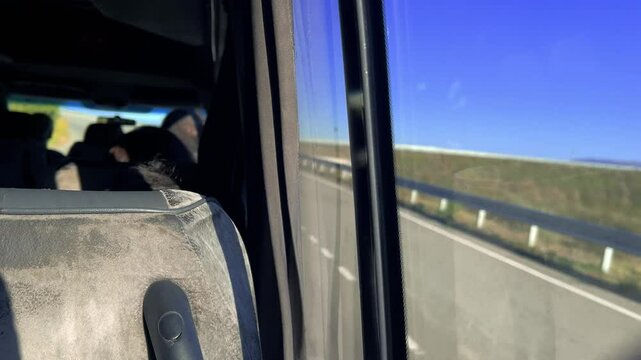 Horizontal 4K video. View from bus window on highway, track, road, tree, grass, bridge, blue sky. Sunny day. Fragment of car interior, chair. Minibus taxi passenger out of focus. Travel, tourism, trip