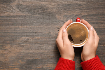 Female hands with cup of coffee on wooden background