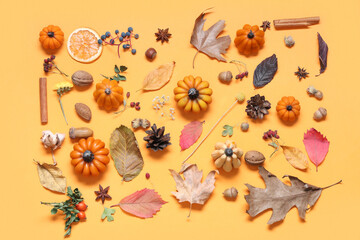 Candles in shape of pumpkin, autumn leaves and berries on yellow background