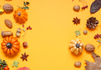 Frame made of candles in shape of pumpkin, autumn leaves and berries on yellow background