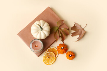 Candles with book, dried orange slices and autumn leaves on beige background